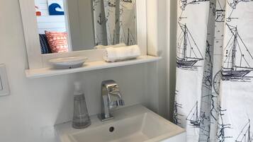 Une salle de bain avec un lavabo blanc, un miroir au-dessus et une étagère sur laquelle est posée une serviette.