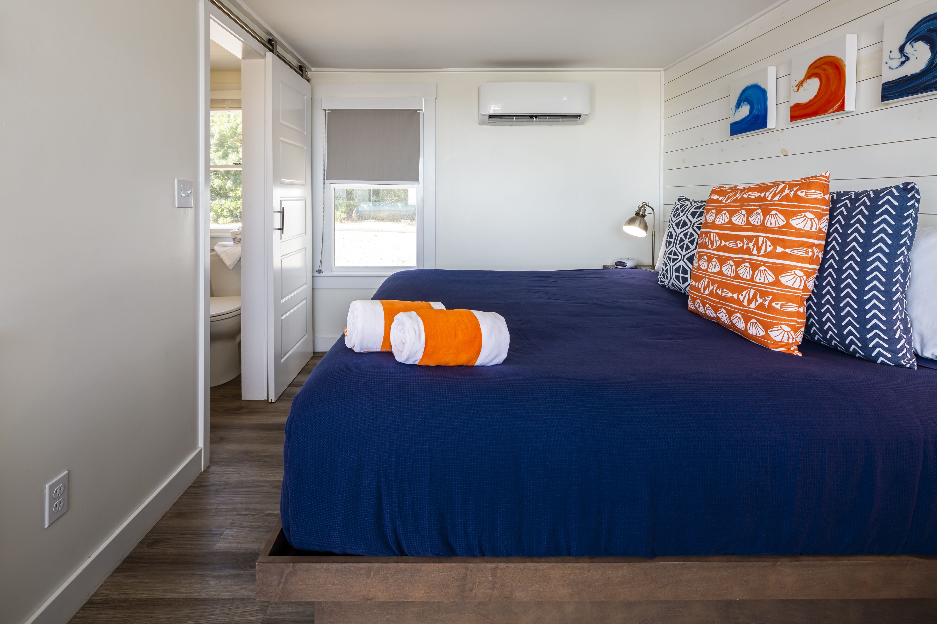 A bedroom with a bed, pillows, a nightstand, a wall-mounted air conditioner, and a window with a view.