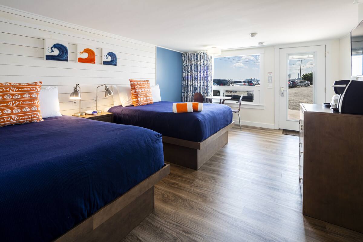 A hotel room with two beds, a desk, and a view of the parking lot.