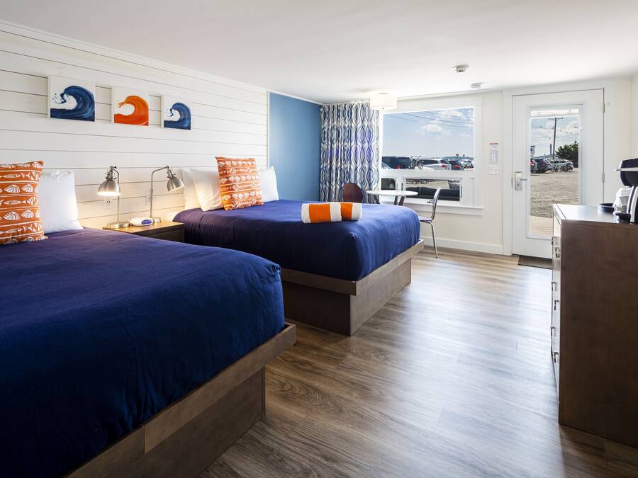 A hotel room with two beds, a desk, and a view of the parking lot.