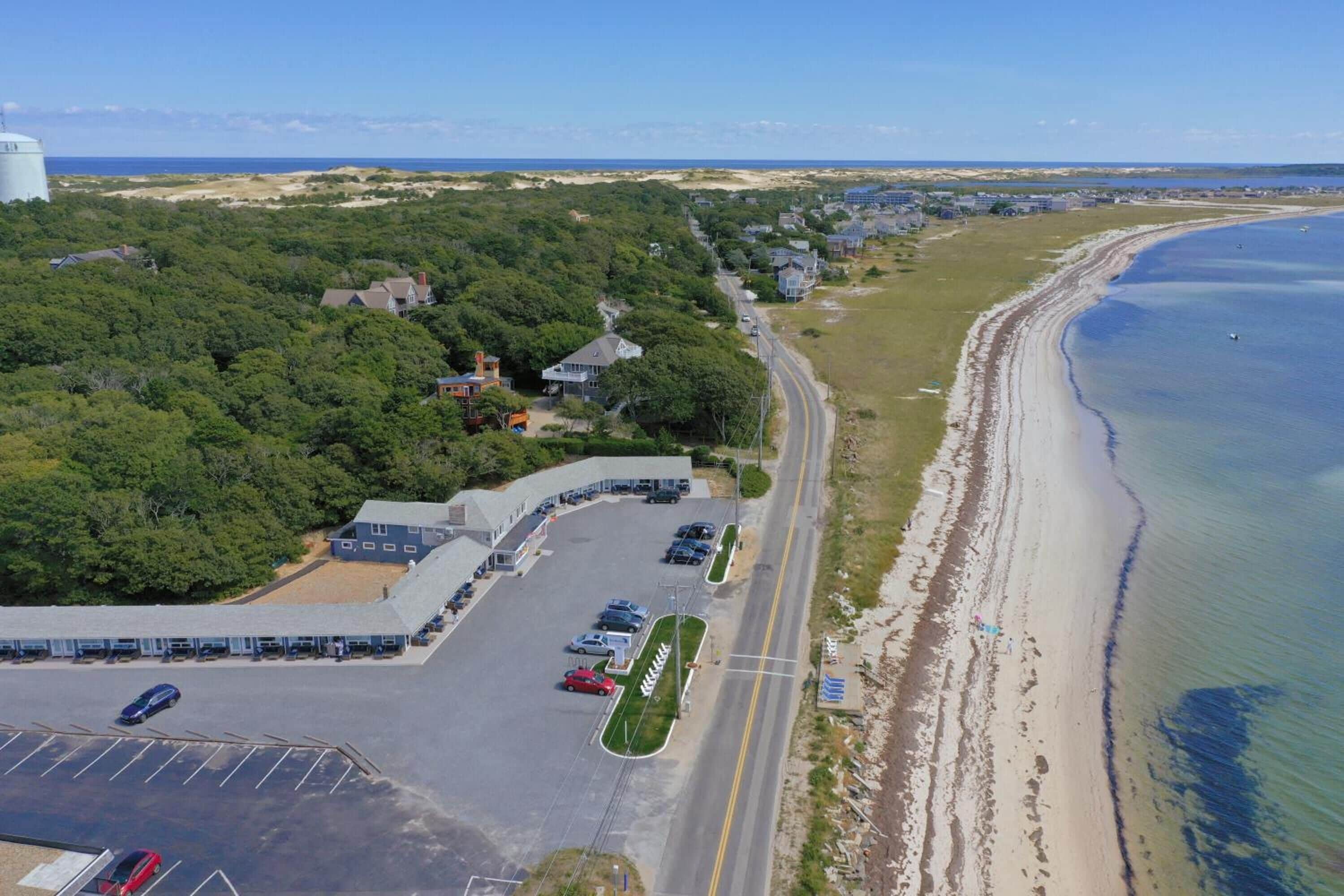 Luchtbeeld van een kustgebied met een parkeerplaats, gebouwen en een strand.