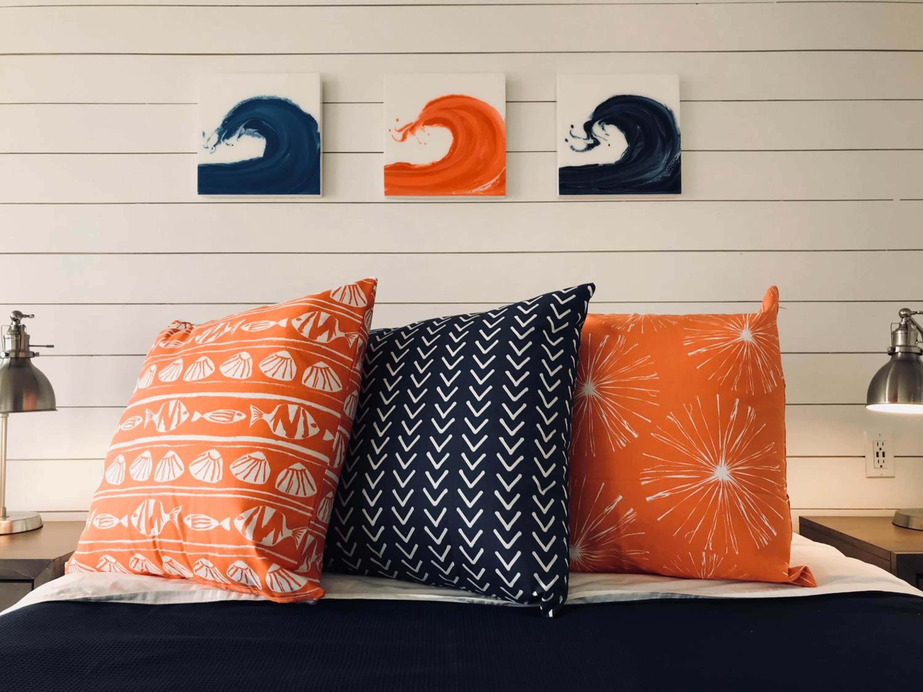 A bed with three pillows and three wall art pieces.