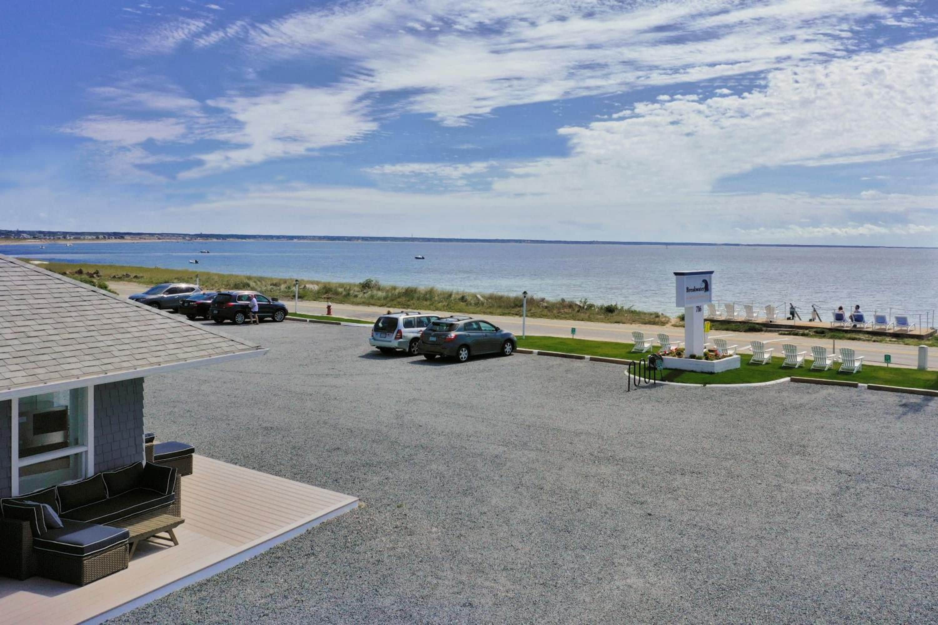 Un'area di parcheggio con auto, vista sulla spiaggia e un cartello che indica una località sul mare.