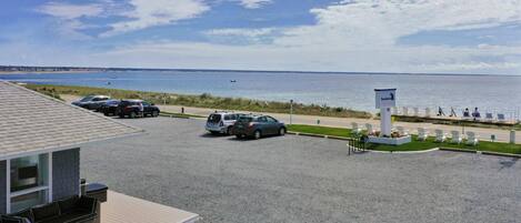 Un'area di parcheggio con auto, vista sulla spiaggia e un cartello che indica una località sul mare.
