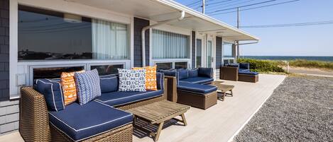 A covered outdoor seating area with wicker furniture and cushions, overlooking a beach.