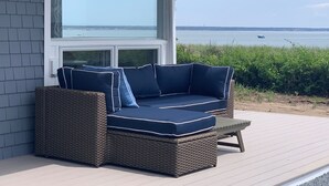 A wicker sofa with blue cushions on a wooden deck, overlooking a body of water. - Breakwater Hotel (Provincetown)