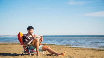 Eine Person sitzt am Strand auf einem Liegestuhl und liest ein Buch.
