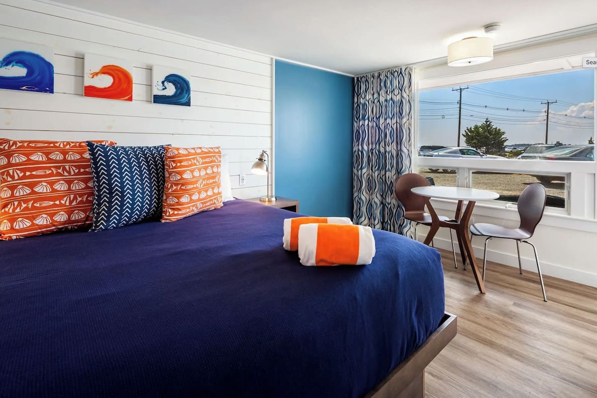 A hotel room with a bed, a desk, and a view of a parking lot.