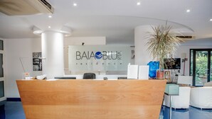 A reception desk with a wooden finish, a large potted plant, and a sign that reads "BAIA BLU residence". - Baia Blu Rta (Lerici)