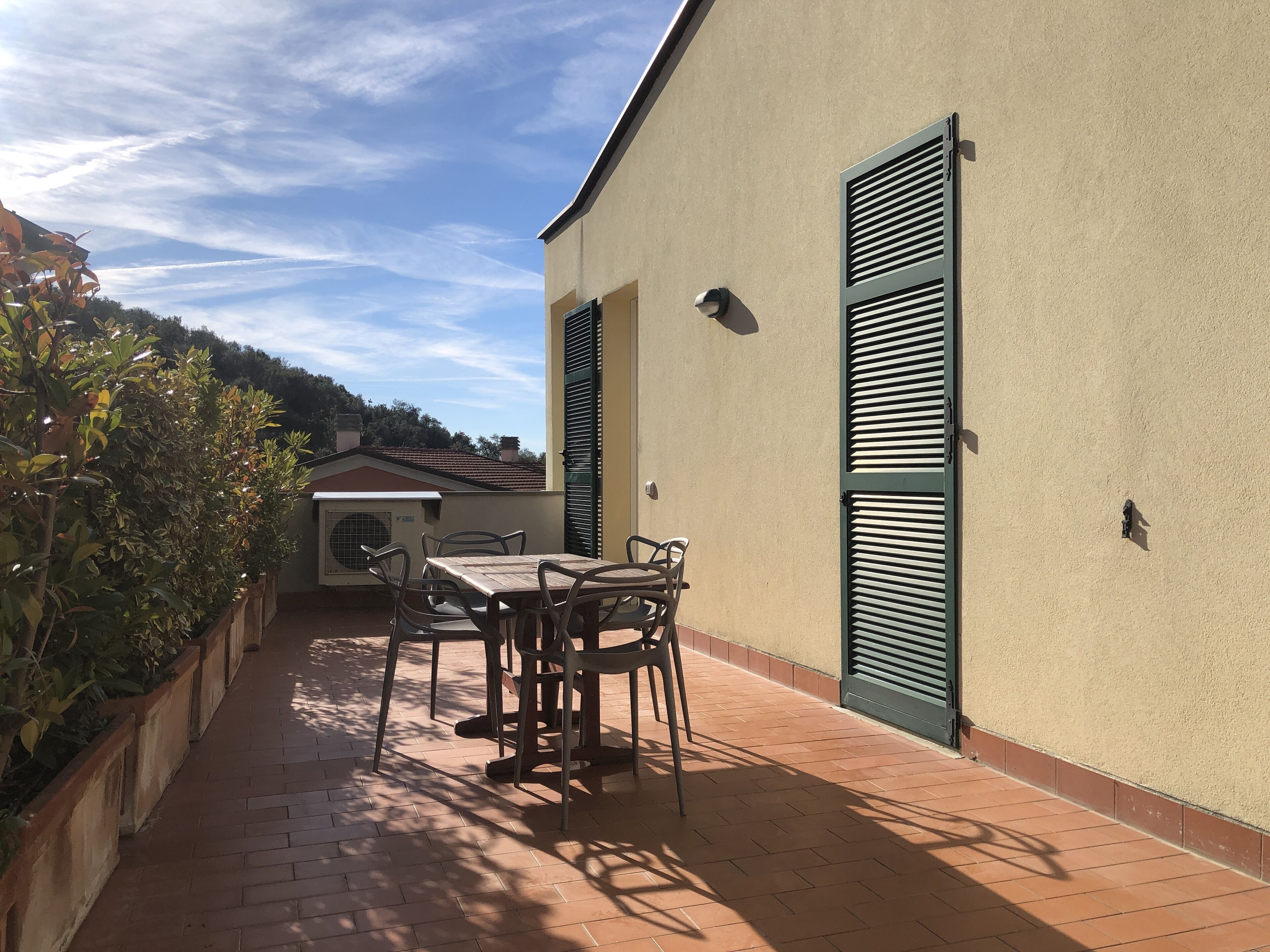 An outdoor patio with a table and chairs, a small air conditioning unit, and a green shuttered door.