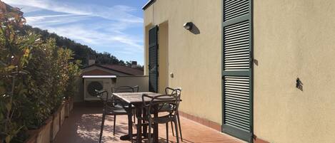 An outdoor patio with a table and chairs, a small air conditioning unit, and a green shuttered door.