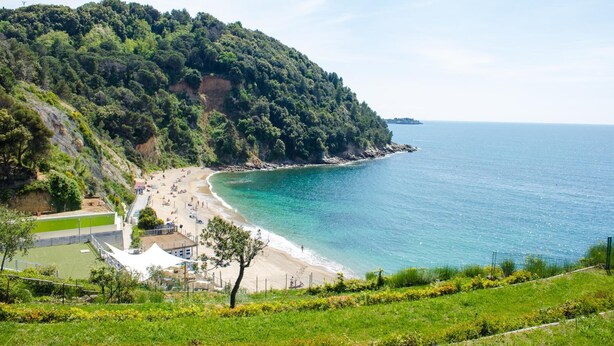 A coastal beach with a cliff, a tennis court, and a fenced area. - Baia Blu Rta (Lerici)