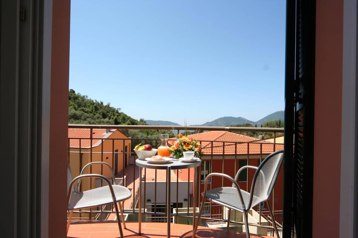 Un balcón con dos sillas, una mesa con fruta y una bebida, y vistas a edificios y colinas.