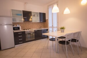 A modern kitchen with a refrigerator, microwave, stove, and cabinets. There is a dining table with chairs and a potted plant.