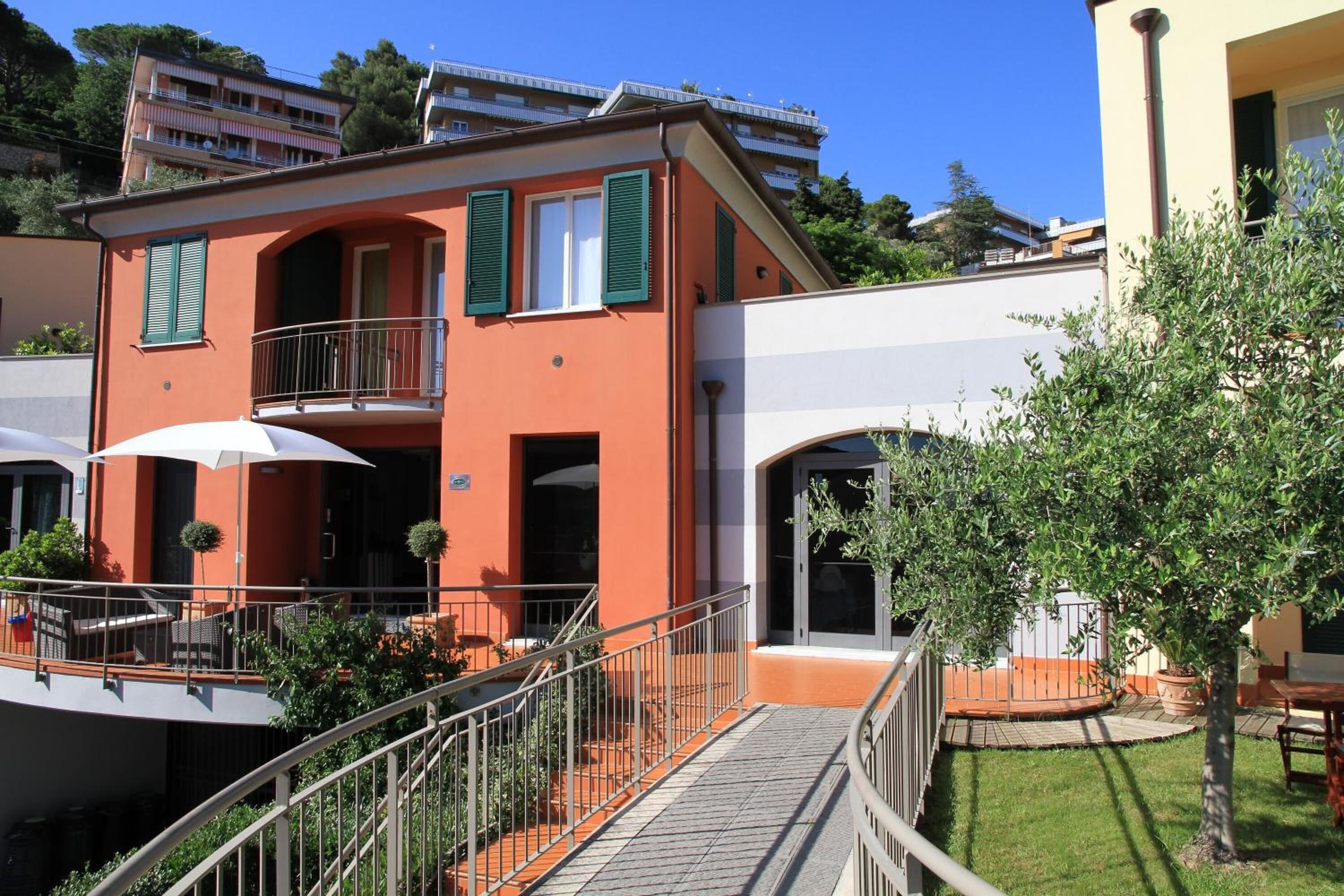 Ein zweistöckiges Gebäude mit Balkon, Außenbereich zum Sitzen und einem kleinen Garten.