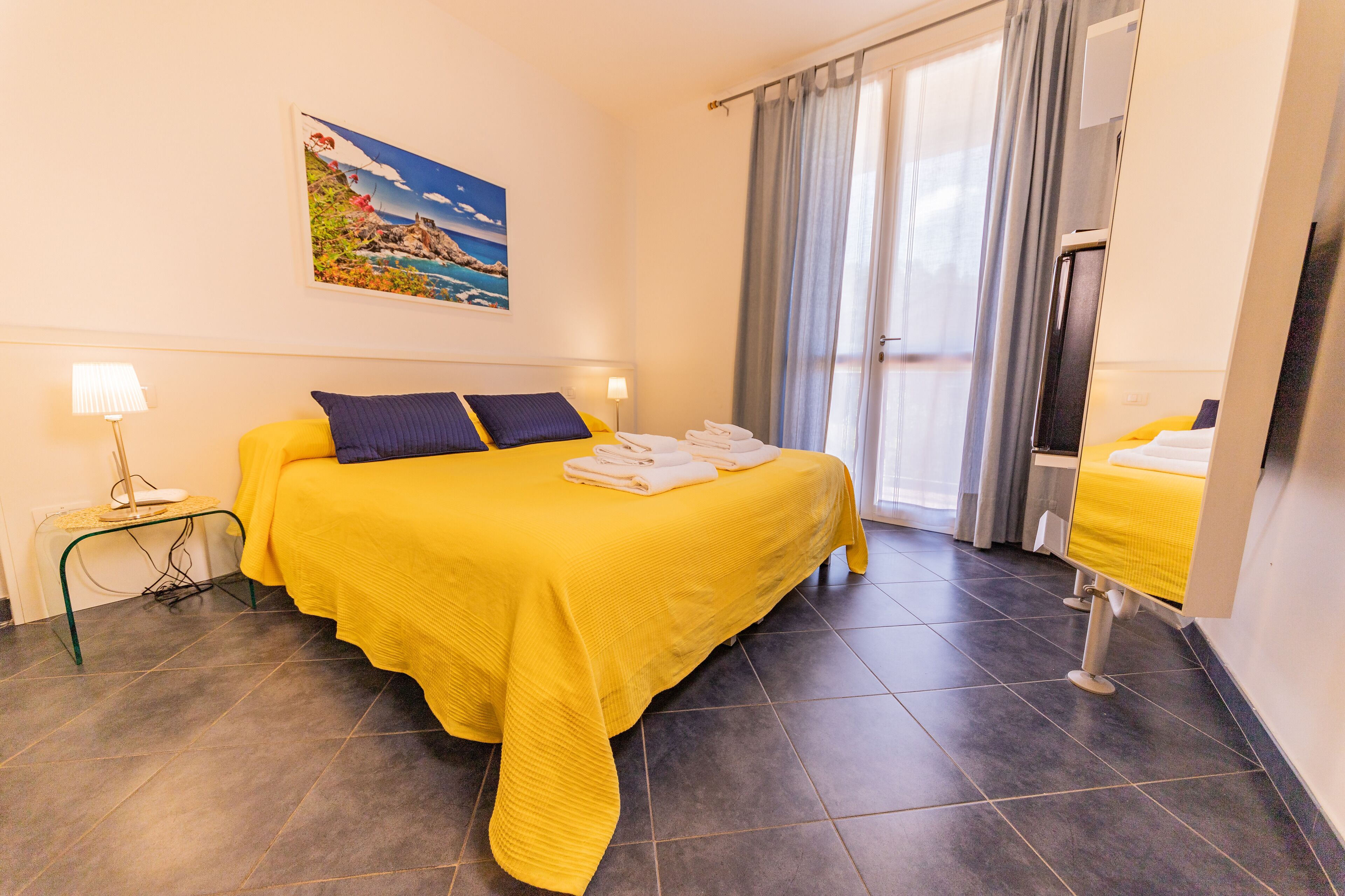 Une chambre d’hôtel avec un lit, un bureau, une chaise, une lampe et un tableau au mur.