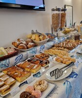 Una mesa de buffet con diversos pasteles y productos de panadería, como cruasanes, pasteles y rosquillas, dispuestos sobre un mantel con diseño azul.