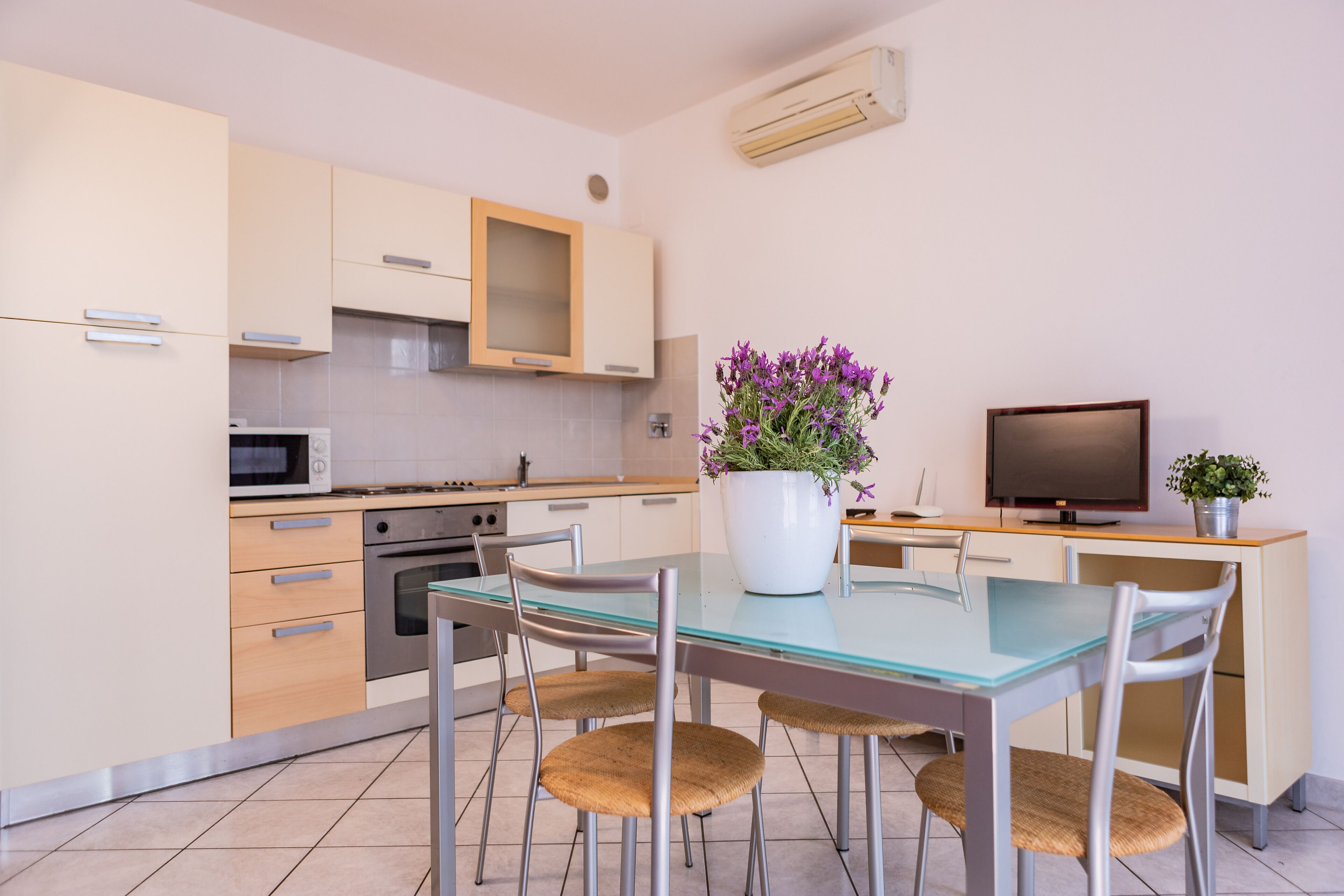 A modern kitchen with a dining area, featuring a glass table, chairs, a microwave, stove, and a TV.