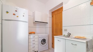 Een compact keuken met een koelkast, een wasmachine en een klein aanrecht met een waterkoker en een bord koekjes.