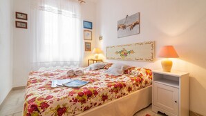 Een net opgemaakt bed met bloemenbeddengoed, een bedlampje en een klein nachtkastje met een lamp.