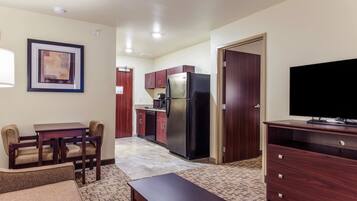A compact living space with a kitchenette, a dining area with a table and chairs, a flat-screen TV on a wooden stand, and a framed picture on the wall.