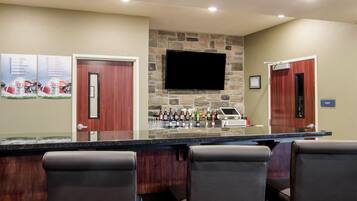 A bar area with a stone wall, a flat-screen TV, and a variety of bottles. There are four bar stools and a counter with a glass display.