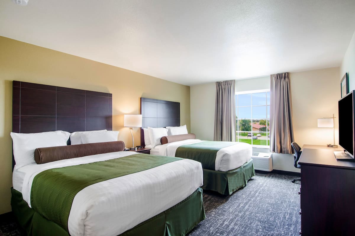 A hotel room with two beds, a desk, a TV, and a window with curtains.