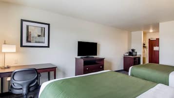 Ein Hotelzimmer mit zwei Betten, einem Schreibtisch, einem Sessel, einem Fernseher und einem gerahmten Bild an der Wand.