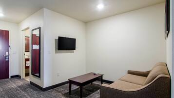 Una habitación pequeña y amoblada con una televisión de pantalla plana montada en la pared, una mesita y un sillón acolchado.