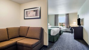 A hotel room with a brown sofa, a bed with green bedding, a desk with a television, and a window with curtains. - Cobblestone Hotel and Suites Torrington (Torrington)