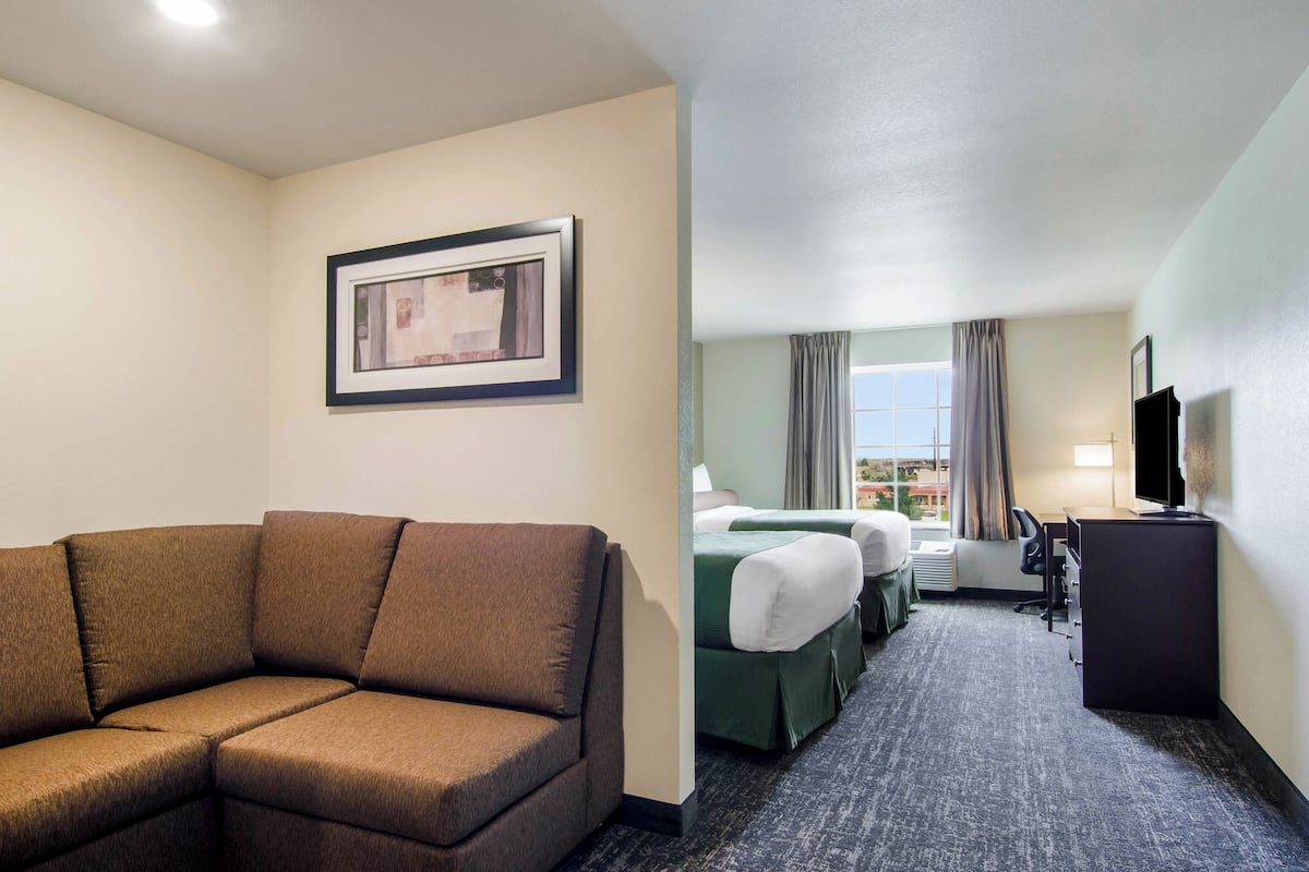 A hotel room with a brown sofa, a bed with green bedding, a desk with a television, and a window with curtains.