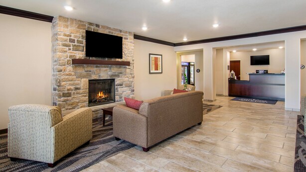A living room with a stone fireplace, a flat-screen TV mounted on the wall, a sofa, and a chair. - Cobblestone Hotel and Suites Torrington (Torrington)