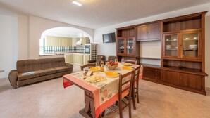 A dining area with a table set for four, surrounded by wooden cabinets and a television mounted on the wall. - Villino Panna (Dorgali)
