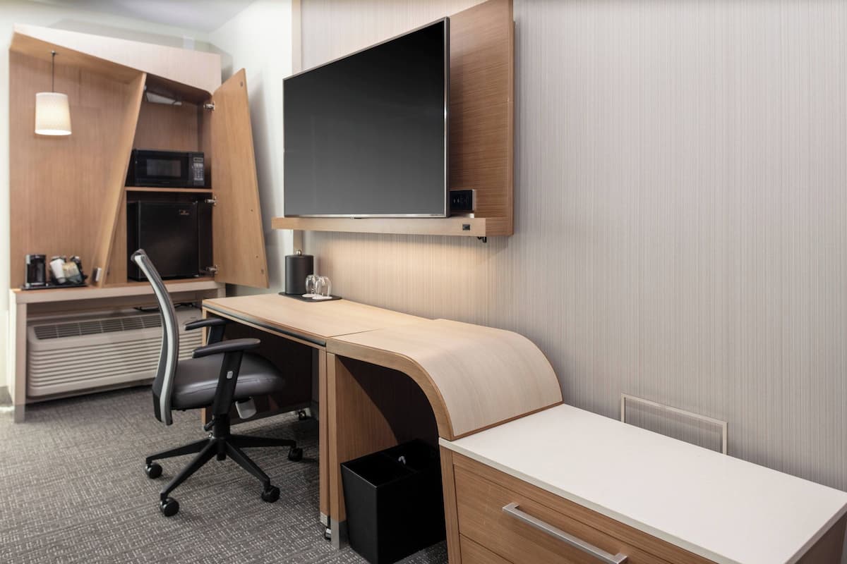 A modern hotel room with a curved desk, a flat-screen TV, a microwave, and a coffee maker.