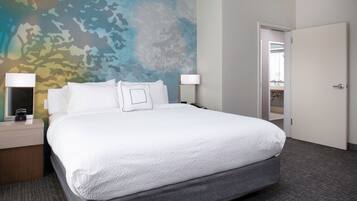 Quarto de hotel com uma cama grande, duas mesas de cabeceira, um criado-mudo, um mural na parede e uma porta para um banheiro.