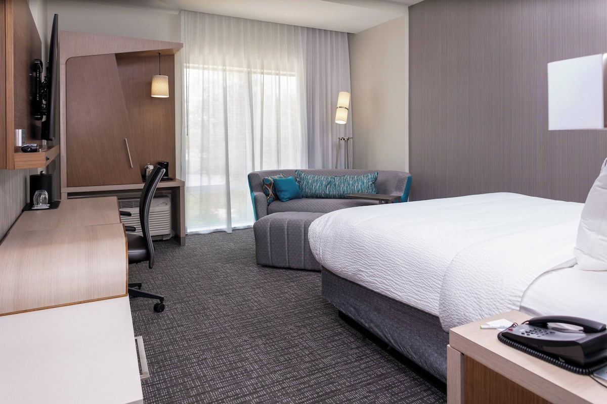 A hotel room with a bed, a desk, a chair, a sofa, and a TV.