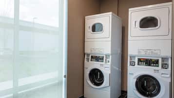 A laundry room with two stacked front-loading washing machines and dryers, a glass door leading outside, and a tiled floor.