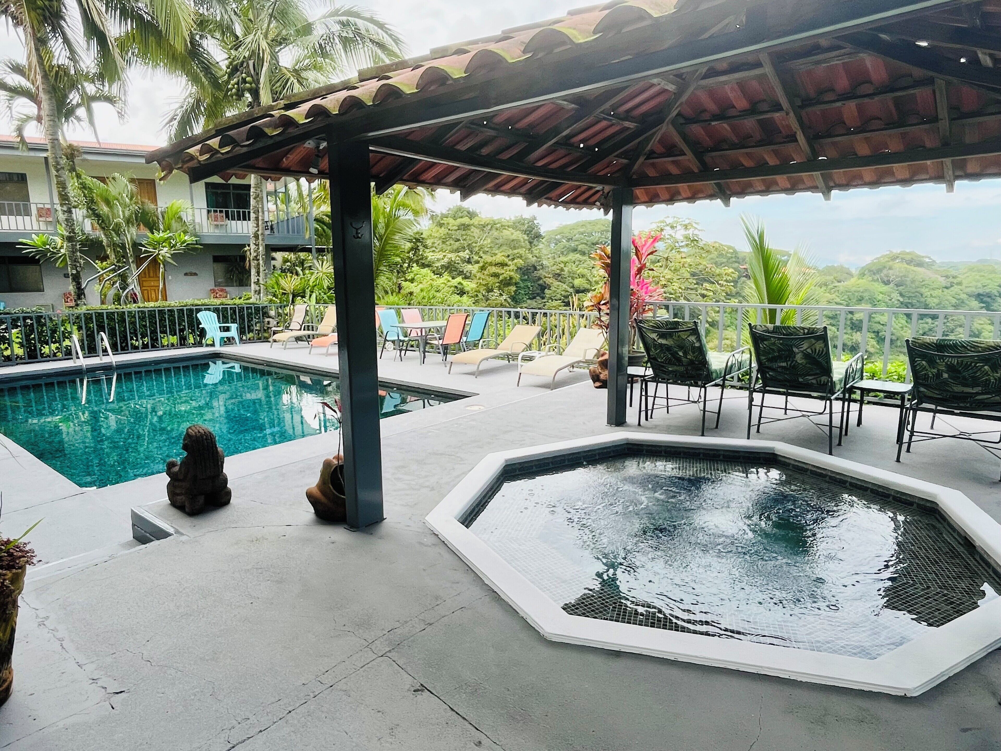 A pool area with a hot tub, lounge chairs, and a covered seating area.