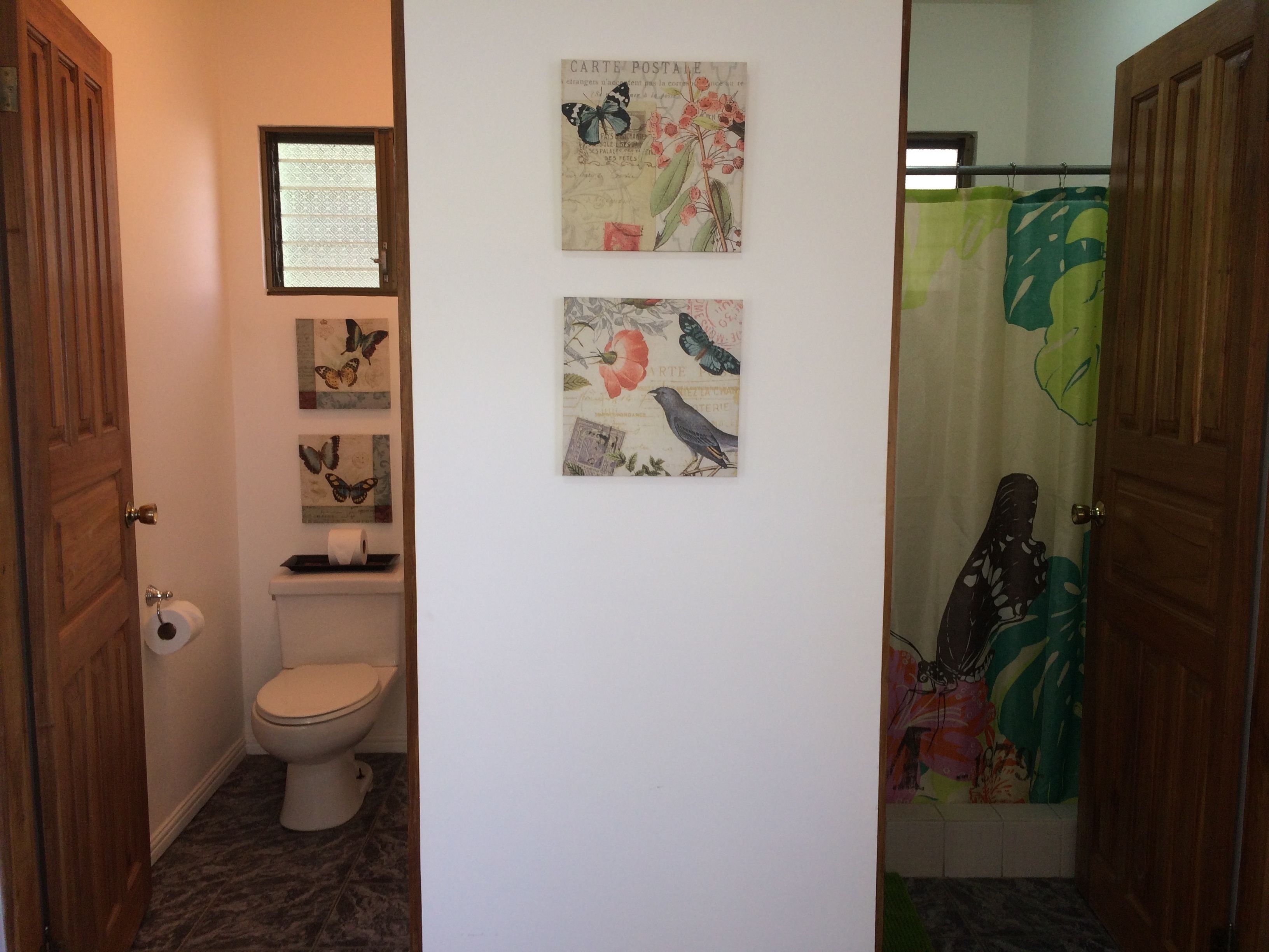 Ein Badezimmer mit Toilette, Duschvorhang und drei Wandbildern mit Schmetterlingen.