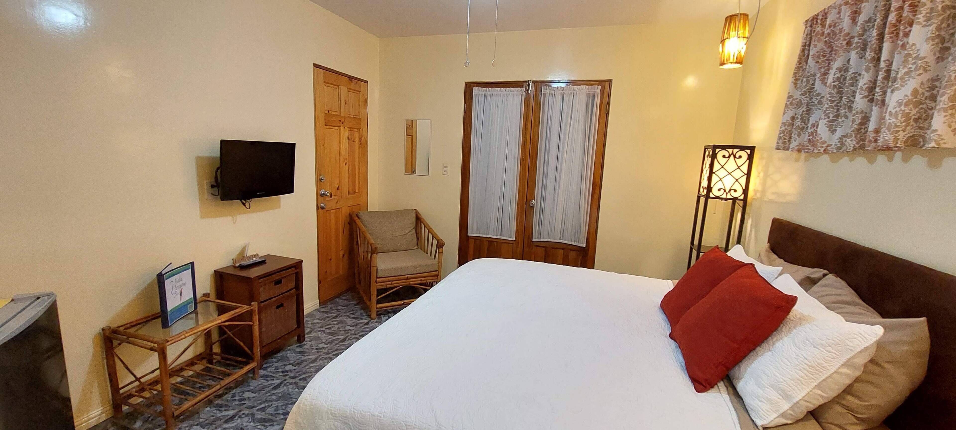 A bedroom with a bed, a television, a chair, a wardrobe, and a bedside table.