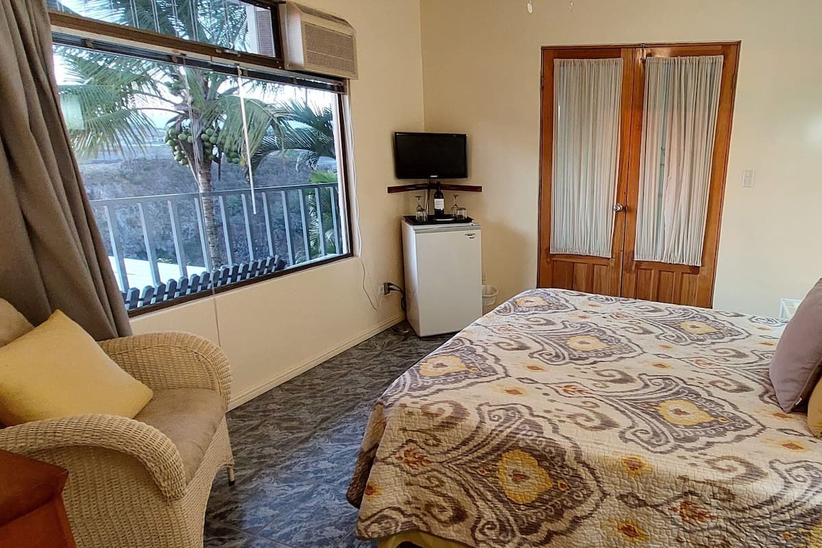 Habitación de hotel con una cama, un refrigerador blanco pequeño, un televisor y una ventana con cortinas.