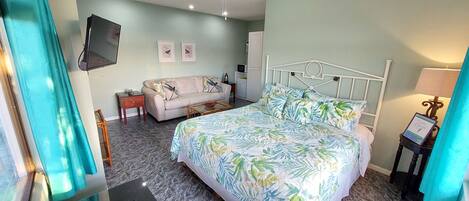 Une chambre à coucher comprenant un lit, un canapé, une petite table, un téléviseur fixé au mur et une lampe.