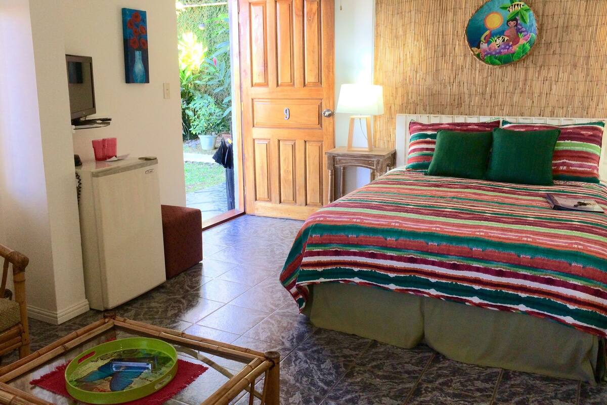 Un dormitorio con cama, mesita de noche, lámpara y vistas al exterior.