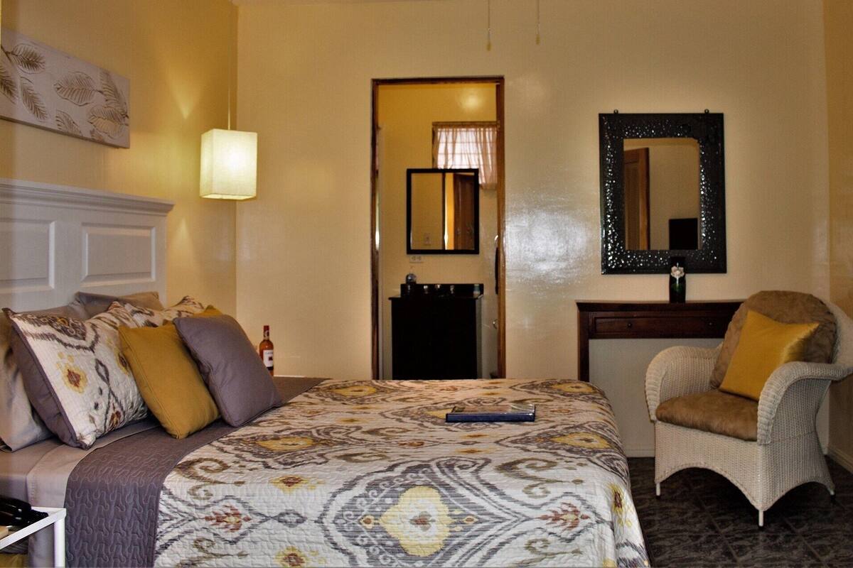 Una habitación de hotel con cama, una silla, un espejo, una lámpara y una puerta.