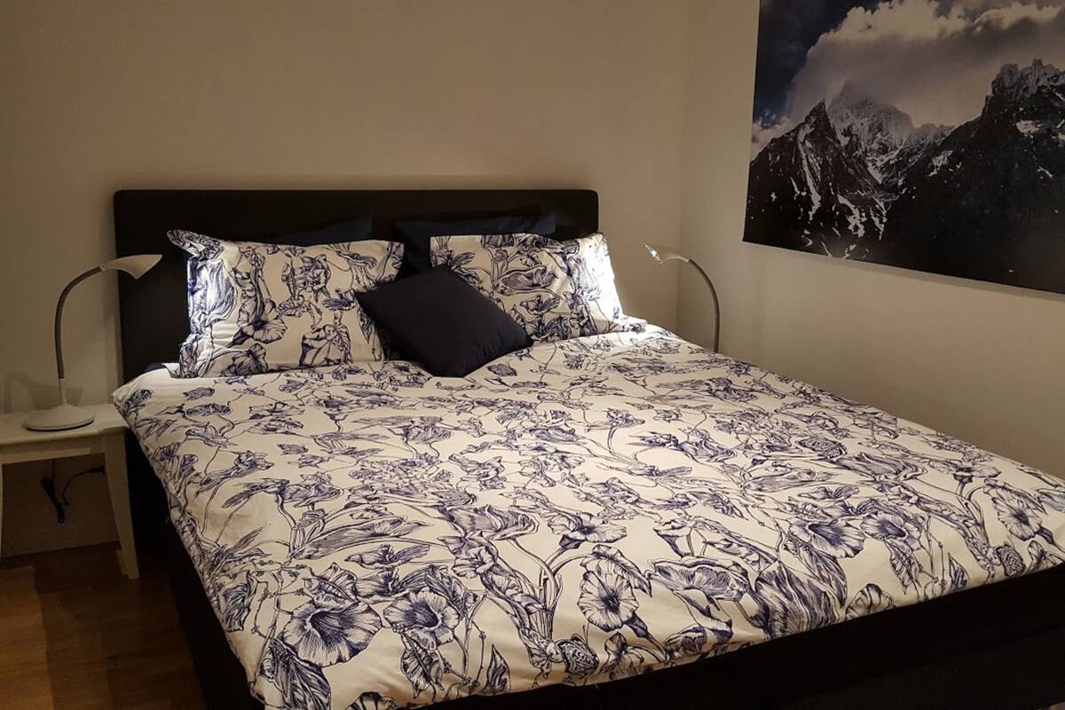 Une chambre à coucher avec une couvre-lit à motifs floraux, une tête de lit sombre et une table de chevet avec une lampe.