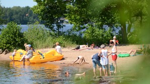 Escena de playa con gente disfrutando de actividades como nadar y remar en bote.