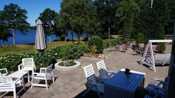 Un patio al aire libre con mobiliario blanco, una mesa cubierta y vistas a un lago.