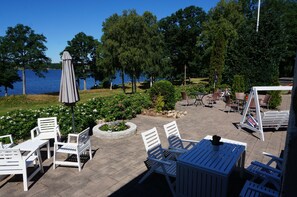 An outdoor patio with white furniture, a covered table, and a view of a lake. - Hägern Bed & Nature (Bolmsö)