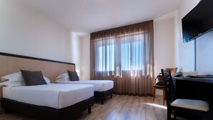 A hotel room with two beds, a desk, a chair, and a TV.