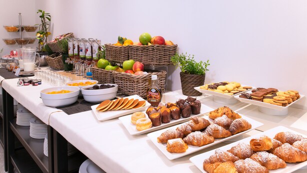 A buffet table with various food items including fruits, pastries, and beverages.